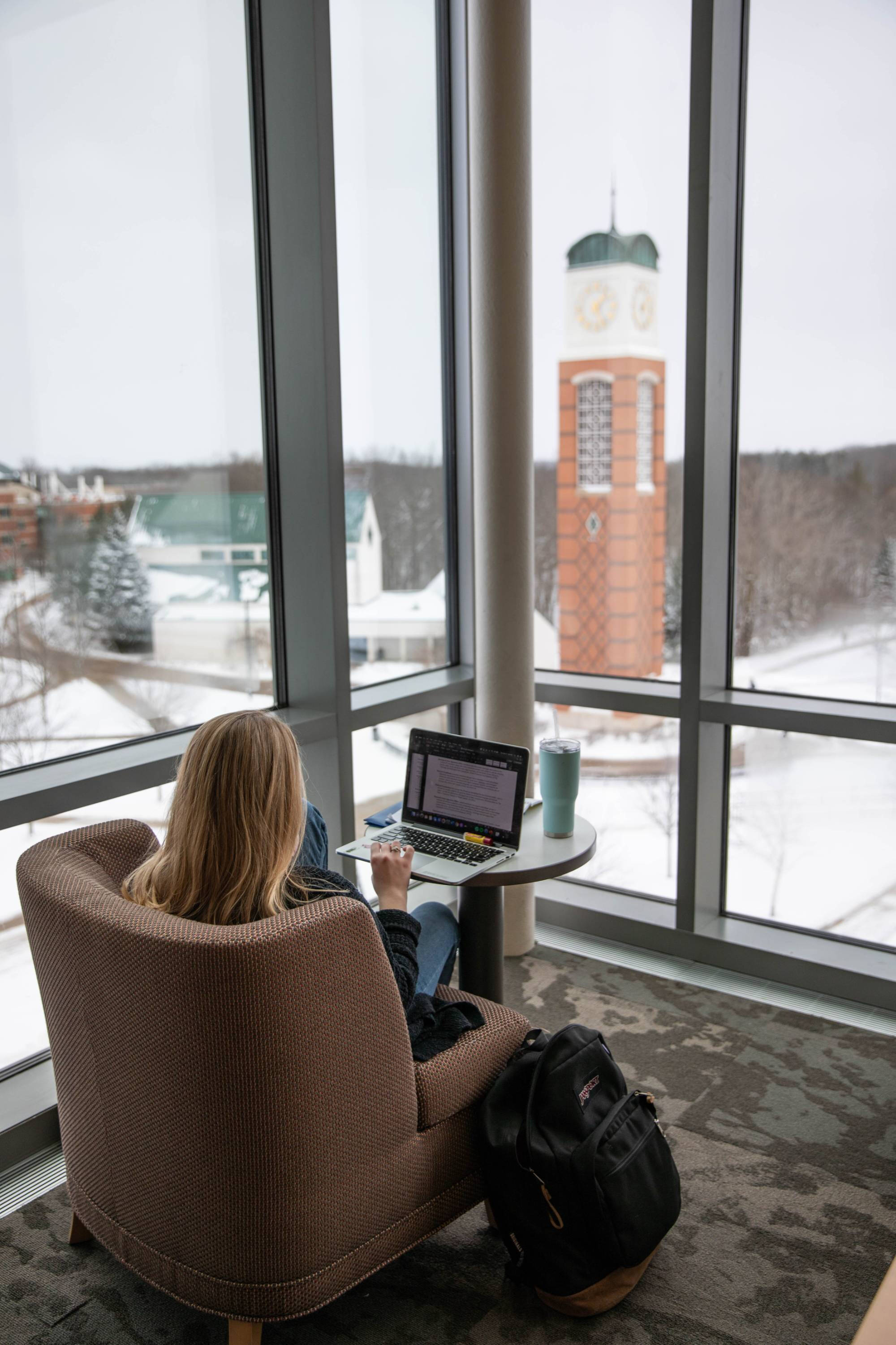 Girl working on a laptop sitting by a glass wall in snowy winter.